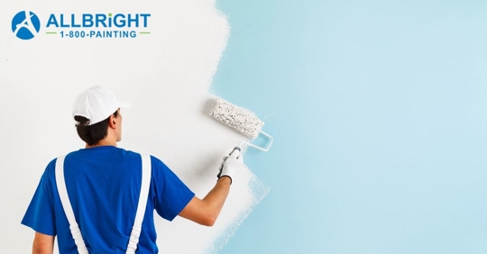 A man in a blue shirt and white overalls painting a wall white