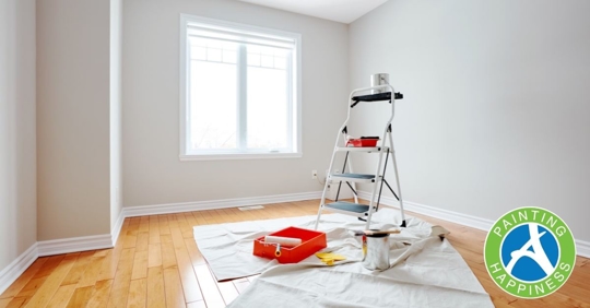 An empty room with a ladder, drop cloth, paint roller, rolling pan, and paint can