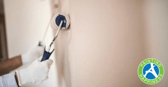 Two paint rollers being held by hands in white gloves placed on a wall