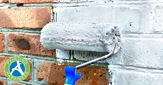 A paint roller with light blue paint on a brick wall